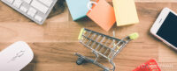 Bird’s eye image of miniature shopping trolley and shopping bags on wooden desktop alongside a keyboard, mouse, and smartphone. Image used to illustrate the SmartFrame Technologies article: ‘Counterfeit goods online: the scale of the problem and how to prevent it’