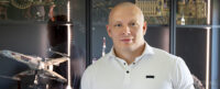 Piotr Kaczmarek in a white shirt stood in front of a lego display.